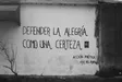 Fotografía en blanco y negro de un muro con la frase «Defender la alegría como una certeza», firmado Acción Poética Mar del Plata