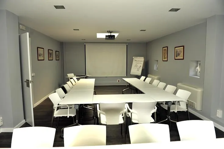 Sala de reuniones con mesas, sillas y pantalla de proyección
